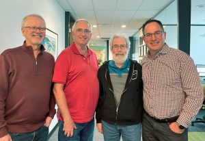 Four men standing in an office hallway.